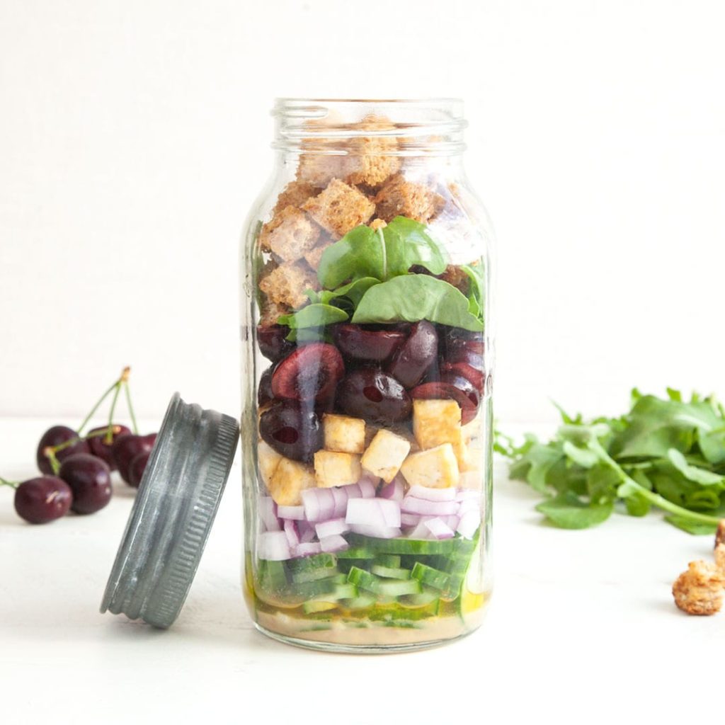 Mason jar salad with cherries, cucumber, onions, spinach, croutons, and dressing.