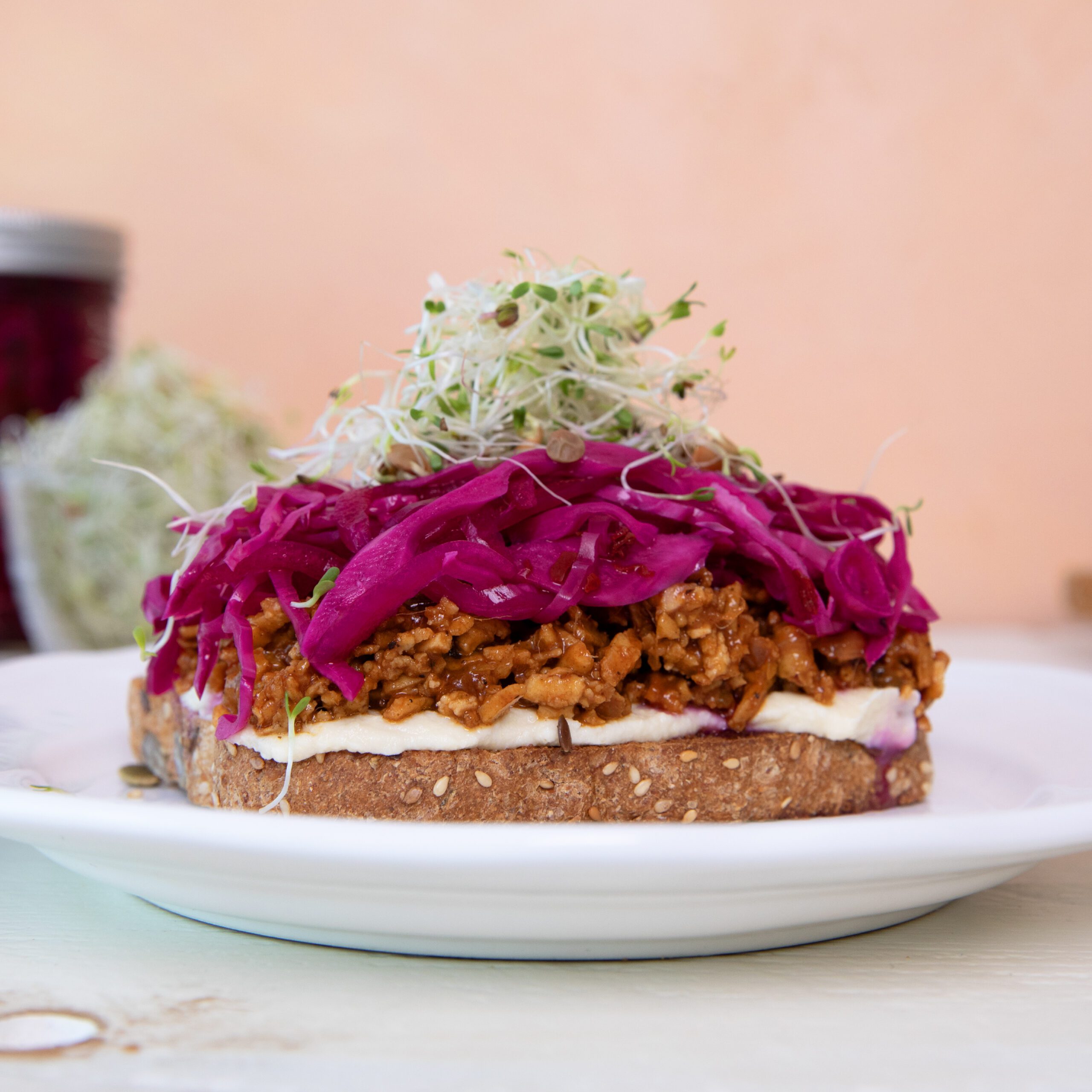 Sweet & Spicy BBQ Shredded Tofu Sandwich with Quick-Pickled Red Onions and Cabbage topped with fresh sprouts without the top slice